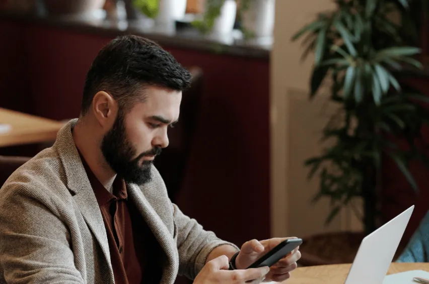 man with pensive look at table with laptop, looking at phone