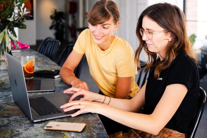 women colleagues looking at shared laptop smiling