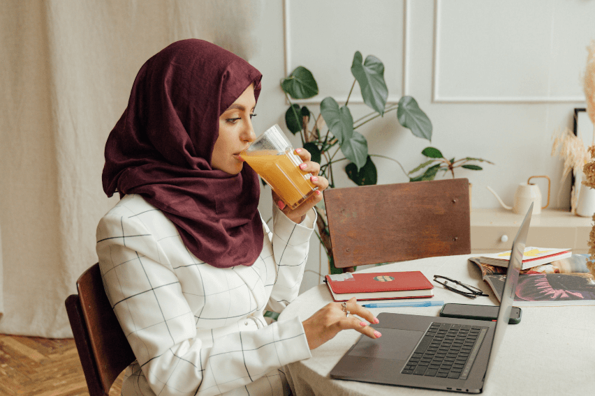 Woman works at laptop while sipping orange juice
