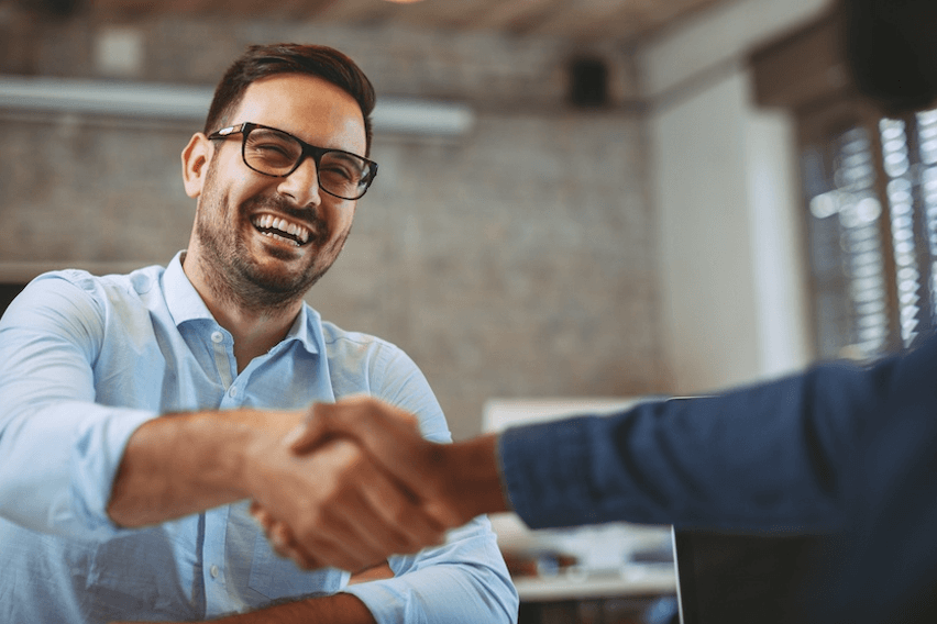 Man wearing glasses smiling while shaking hands with someone out of frame